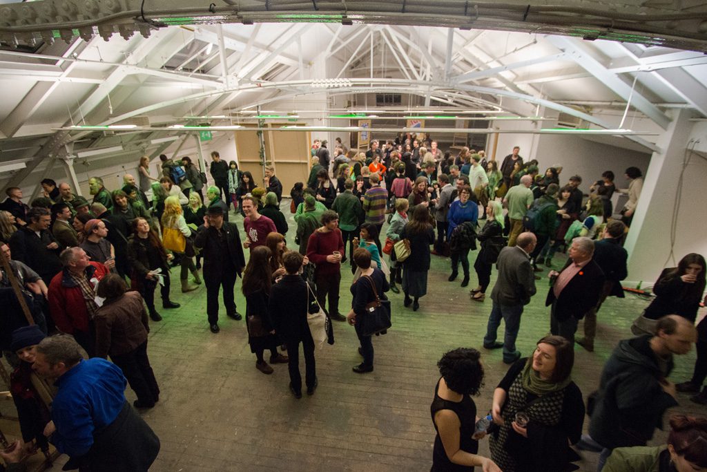 A scene of many people under a plastic canopy. It looks like the preview of an art event.