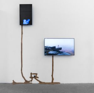 Two screens mounted on a white wall, they are connected by brown parcel tape covering the wires down to the plug.