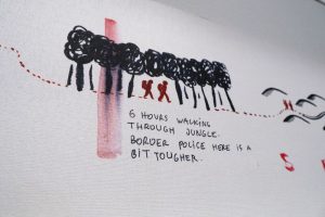 A white wall with black smudgy drawing of figures amongst trees and words underneath.