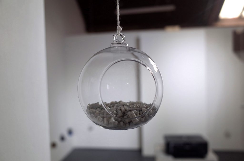 A transparent orb hung at head height in a gallery. Inside the orb is a material that looks like broken up tiny cubes. The orb has a circular hole so that the contents can be touched.