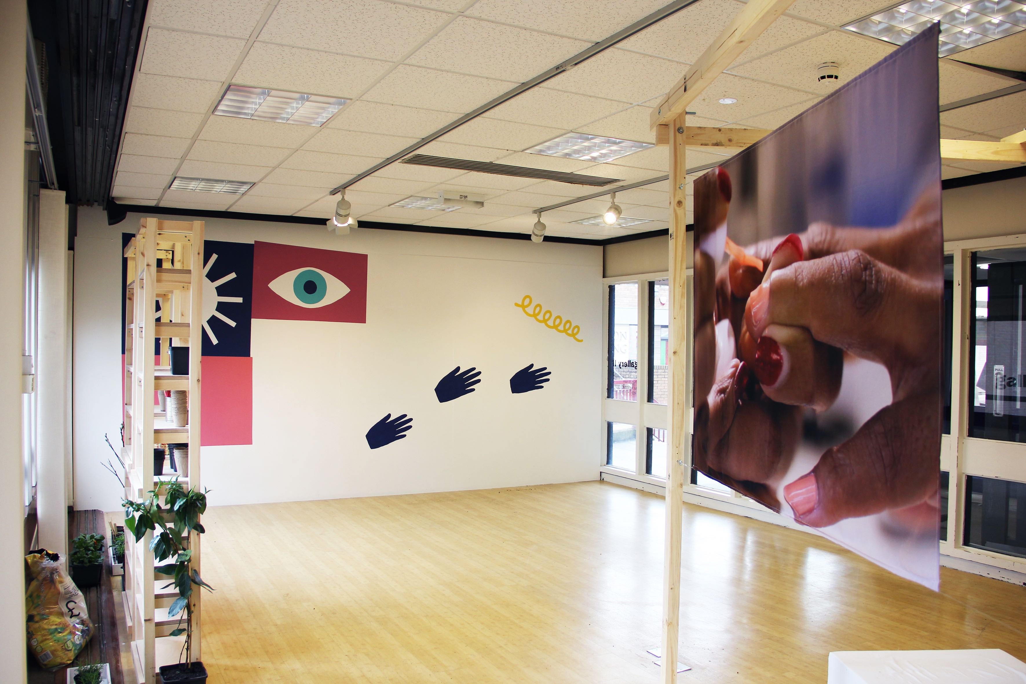 View of a gallery with several works mounted to the walls and hanging from the ceiling, in shades of purple and red.
