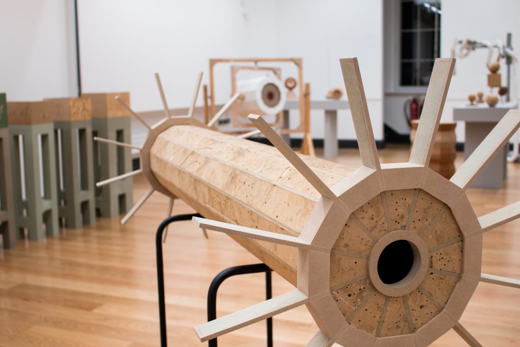 A view of a wooden sculpture that looks like a large cog, resting on a metal frame.