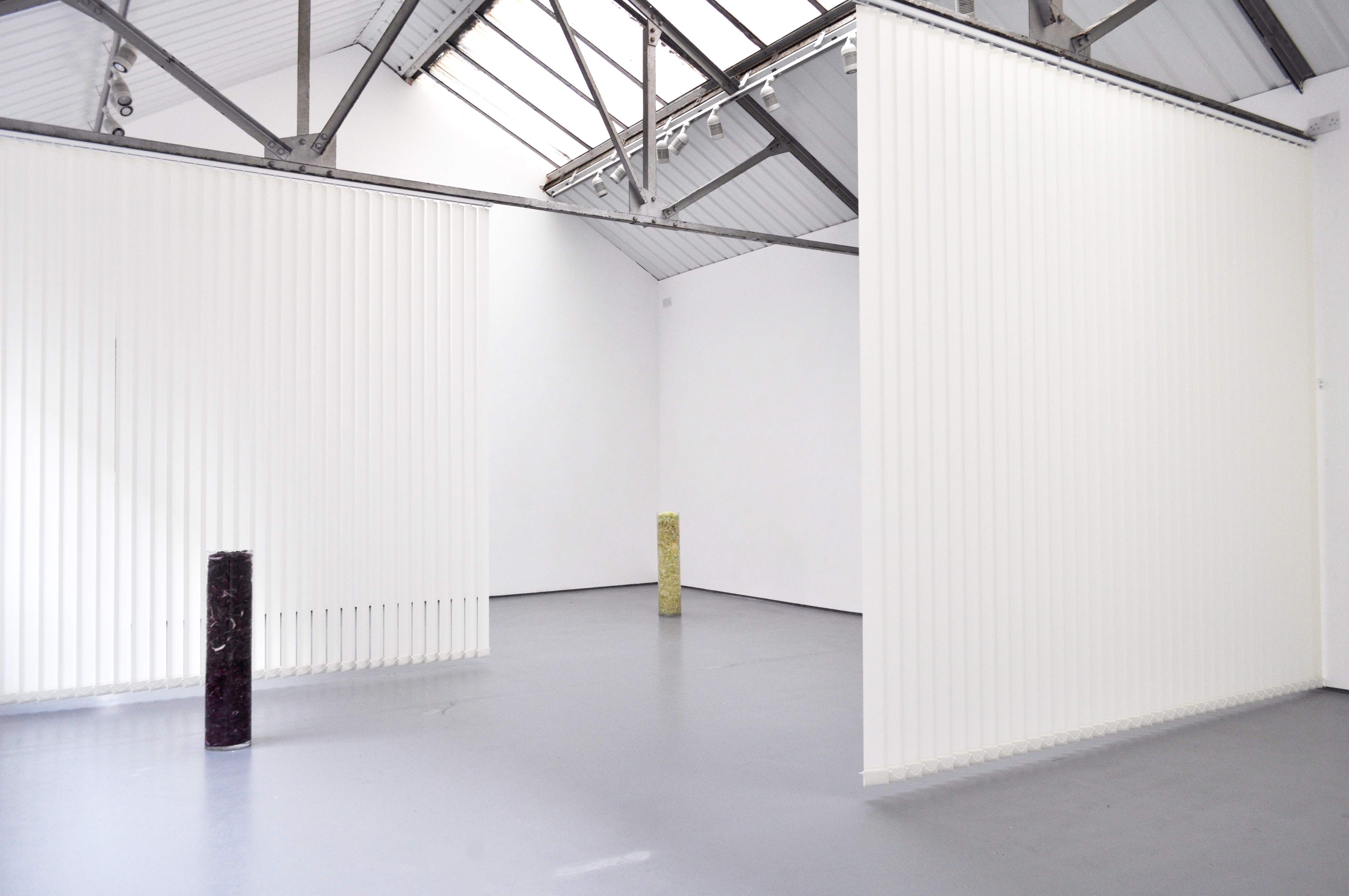 View of a gallery with white walls and grey floor. Several sculptures are visible throughout the space.