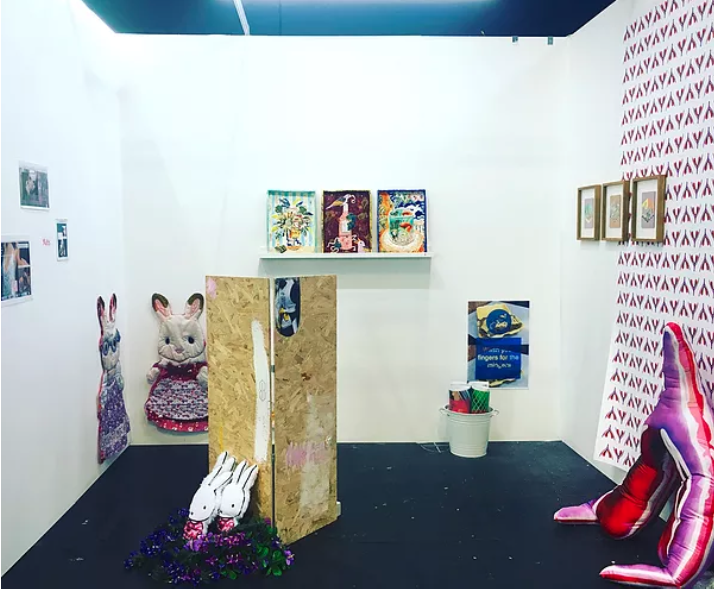 A small white cube space filled with art objects.
