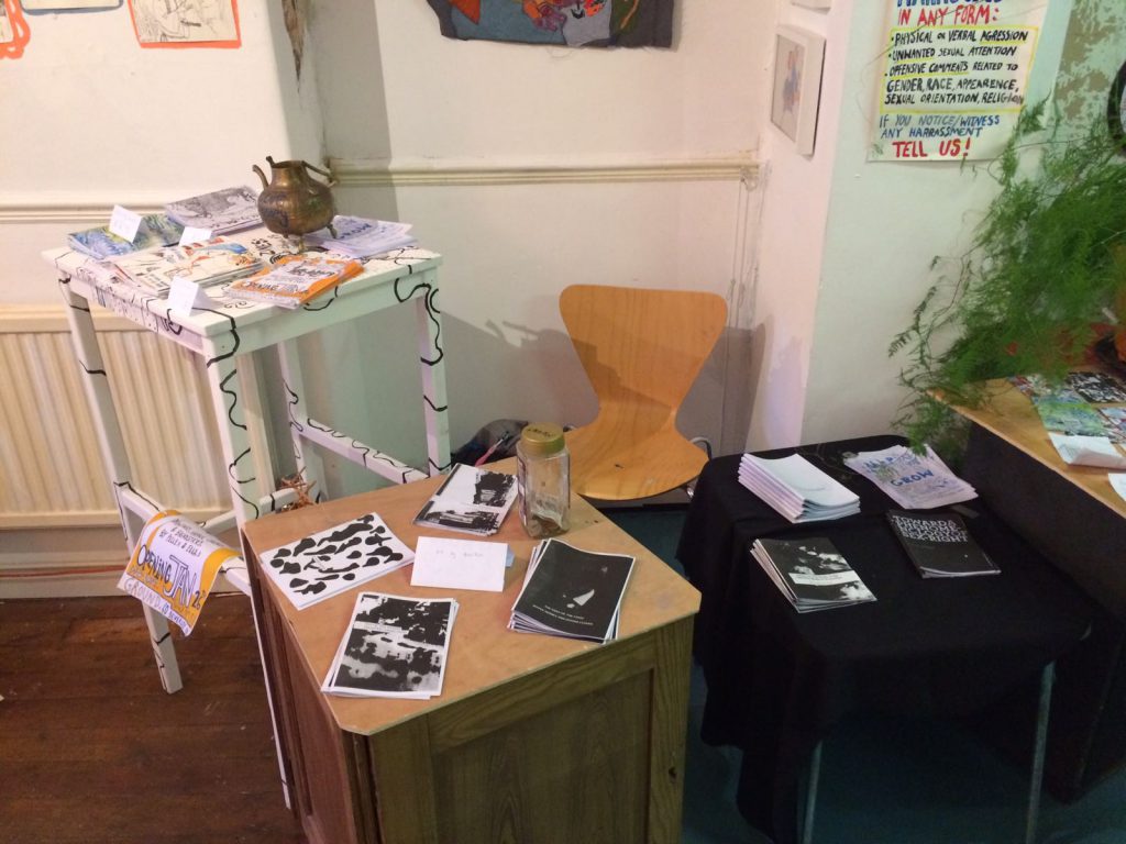 A stall at a zine fair, with several stools and tables holding copies of zines.