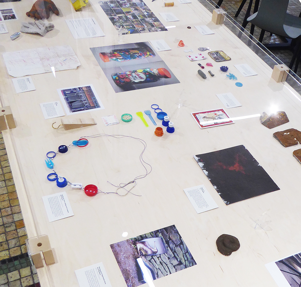 A vitrine containing bits of plastic rubbish and detritus and printed photographs.