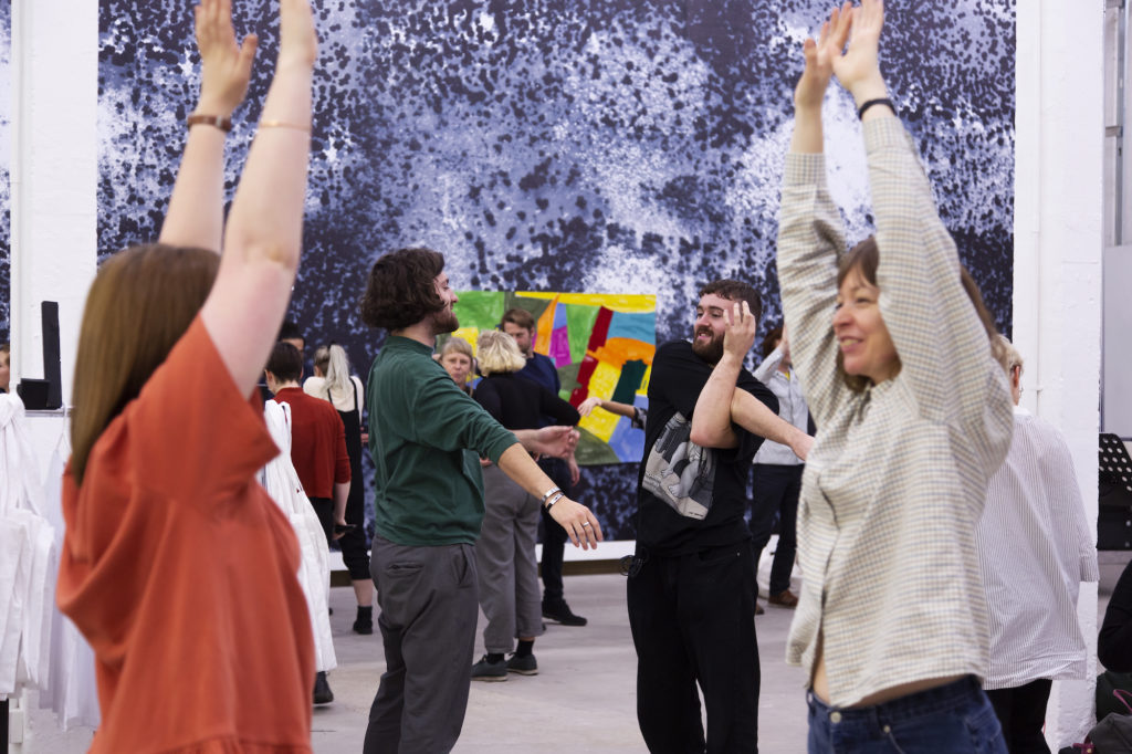 A group of people are stood in a number of poses, smiling, in front of a large screen painted to look like a galaxy in space.