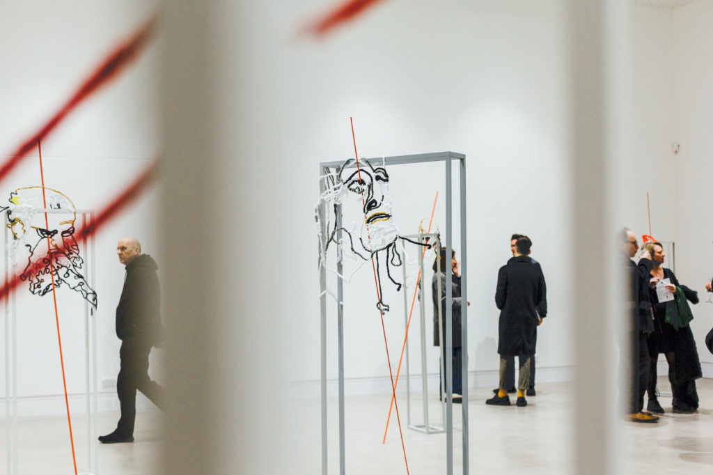 A white gallery space filled with sculptures and visitors.