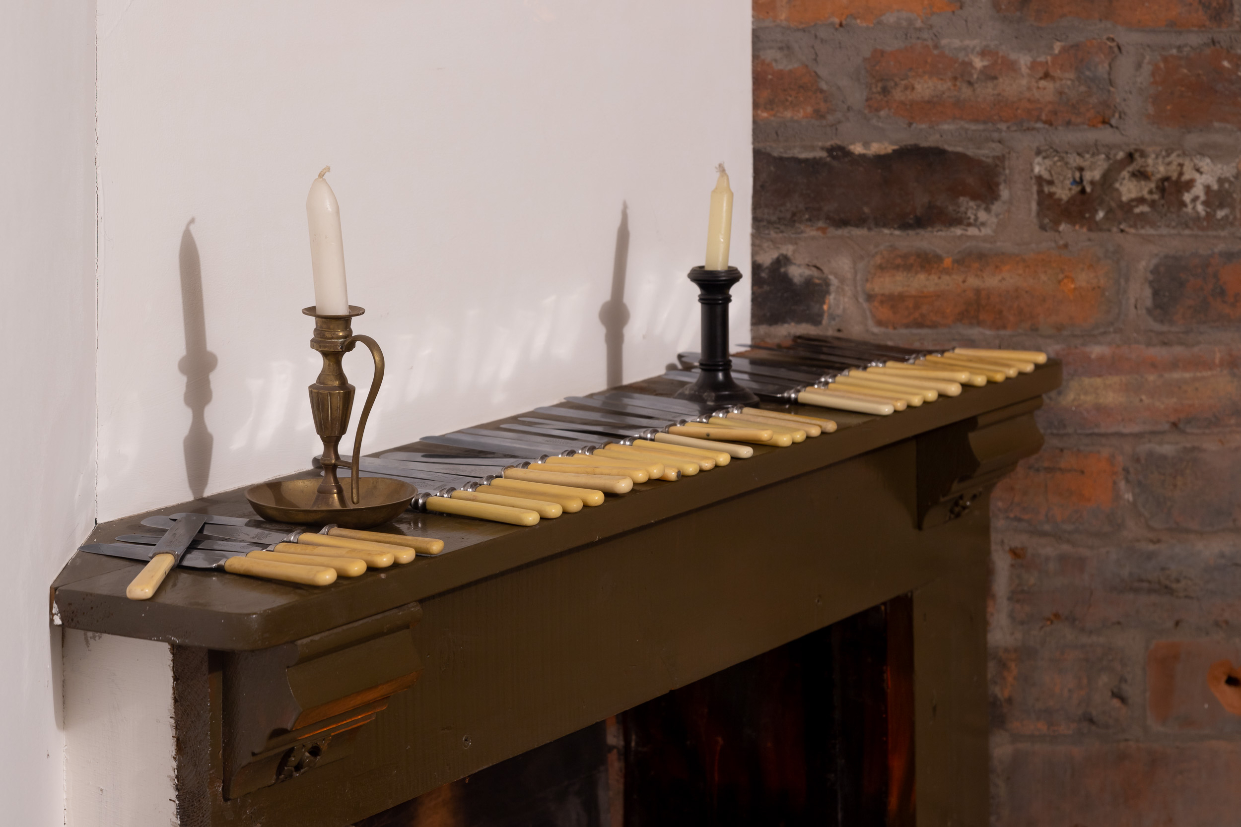 The mantle of a fireplace arranged with a selection of knives and two candlesticks.