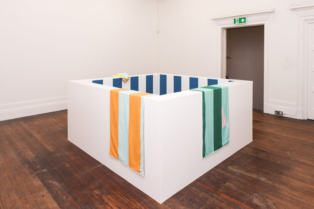 Striped beach towels hang on a low white wall