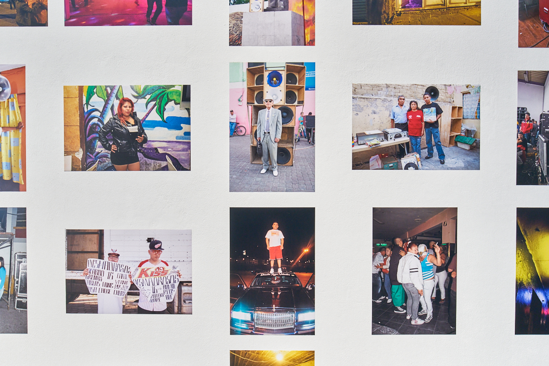 Lots of photographs on a white wall including portraits and candid group shots.