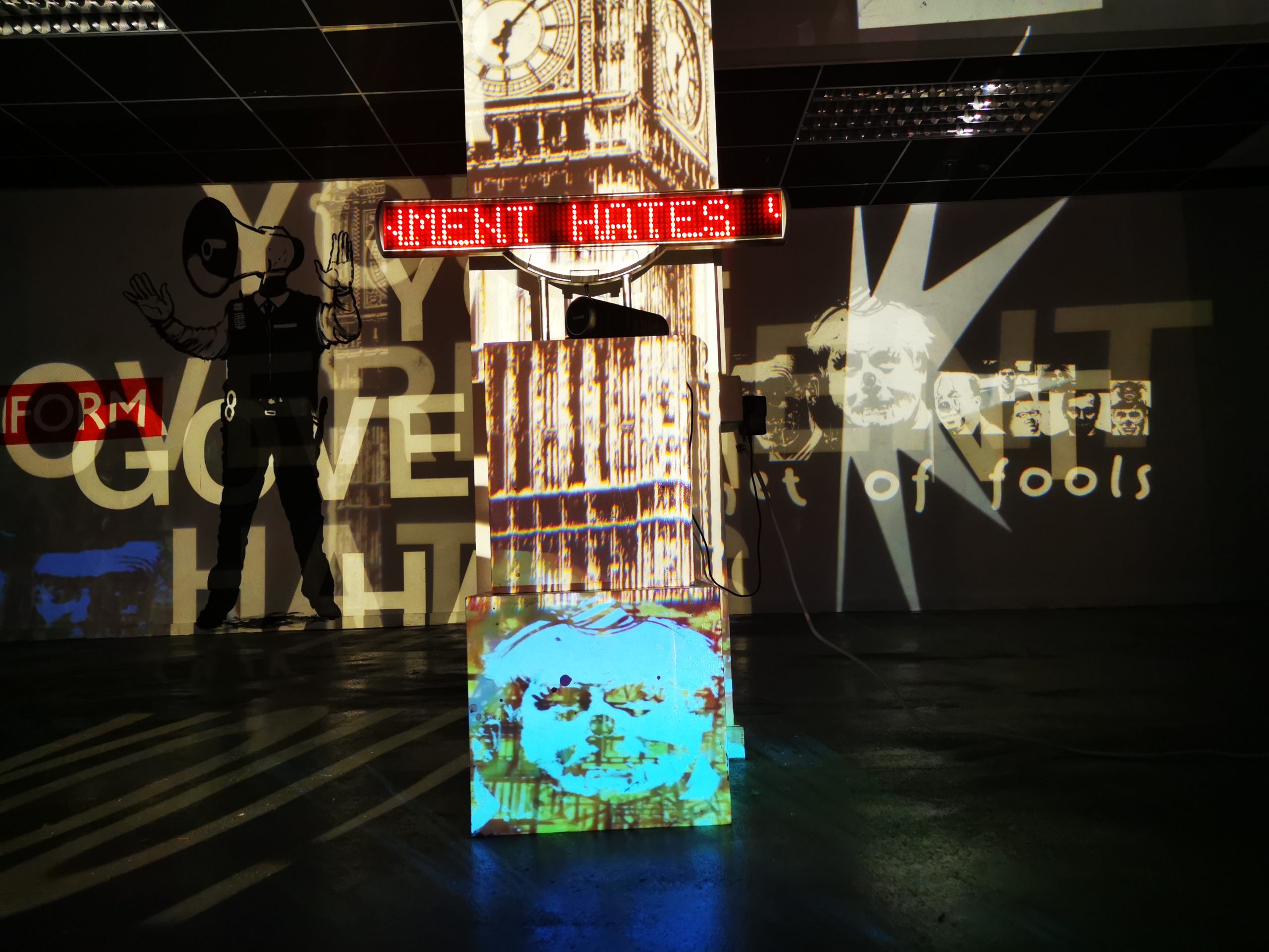 An image of an art installation in a shopping centre. There are a series of projected images and lights in the darkened space.