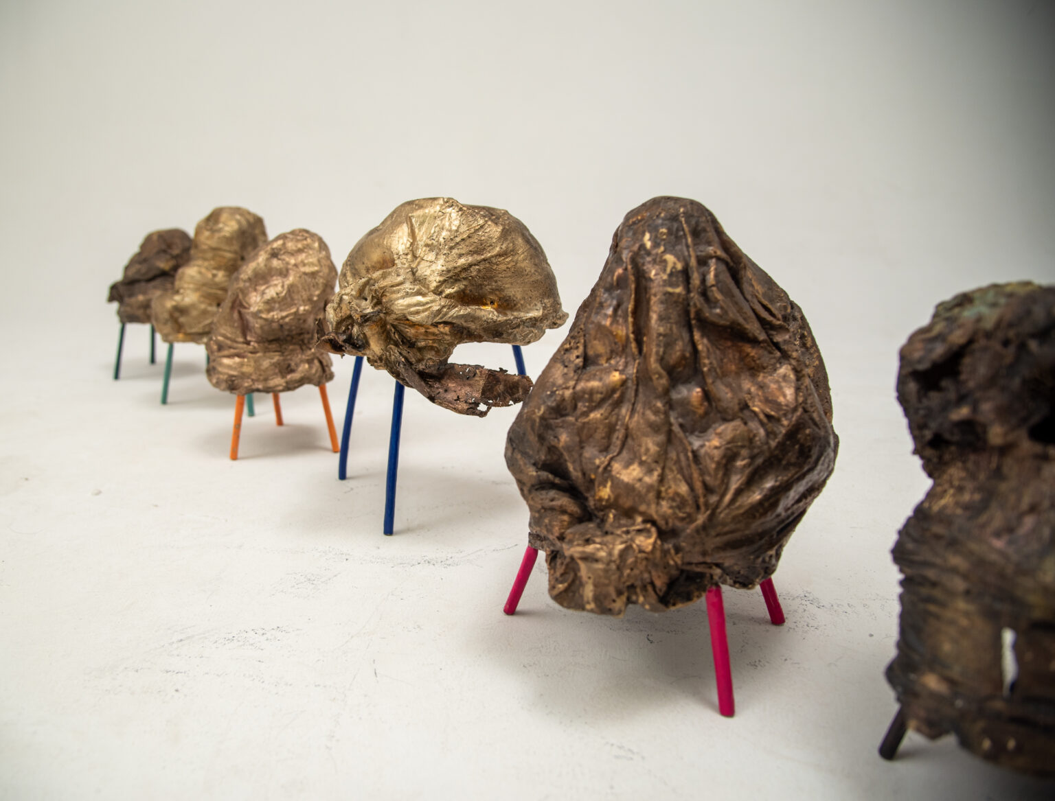 A series of bronze sculptures of elaborate Afro hairstyles for women mounted on short and colourful wooden sticks.