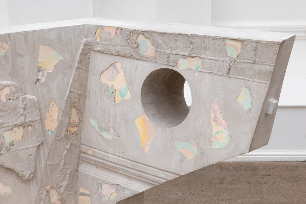 An image showing the detail of one of the sculptures, which appears to be cast. The superficial layer flakes off in places to show a pastel, multi-coloured underlayer