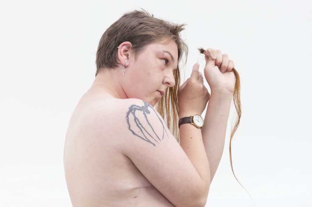 A photo of the artist, shirtless, cutting his long hair away with a scalpel.