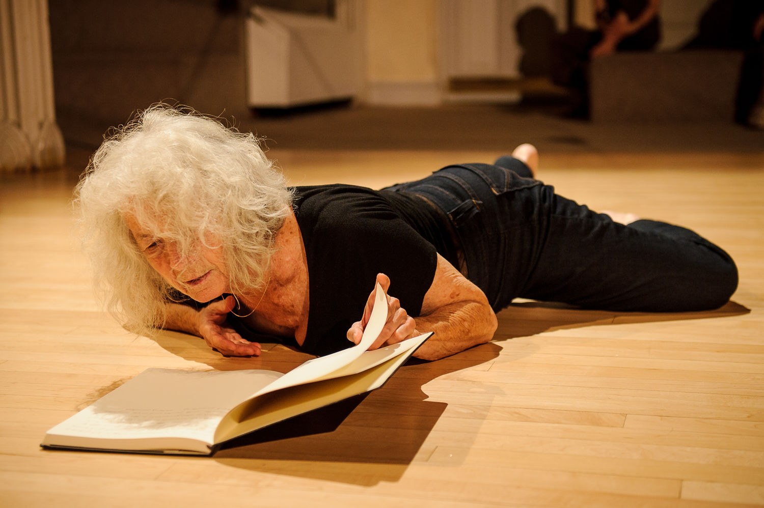 A photo of a woman lying on her front in a studio space, reading from a notebook.