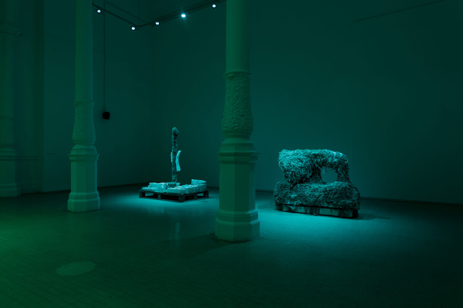 Two sculptures resembling an underwater wreckage sits in the centre of a green-lit gallery space.