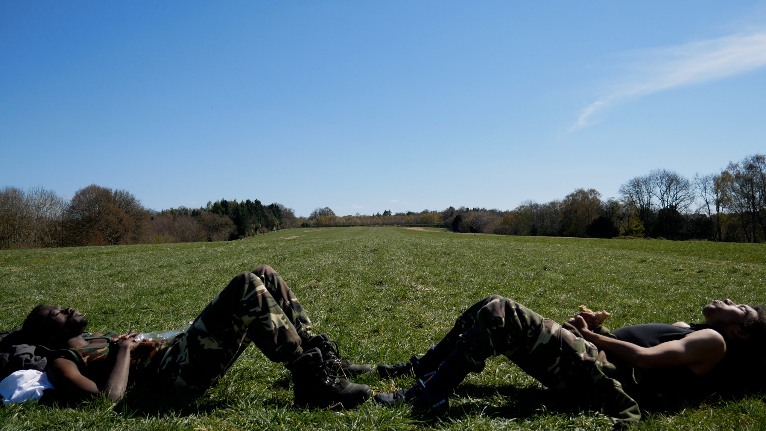 Two people lying toe to toe in a field with their knees bent, a blue sky above them.