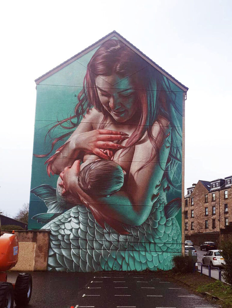 Photo of the side of large mural on the side of a house depicting a mermaid breastfeeding her baby