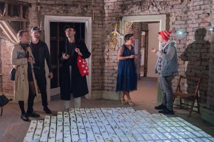A grid of porcelain, gold leafed brickes cover the floor in a red-brick walled room, with viewers standing around talking