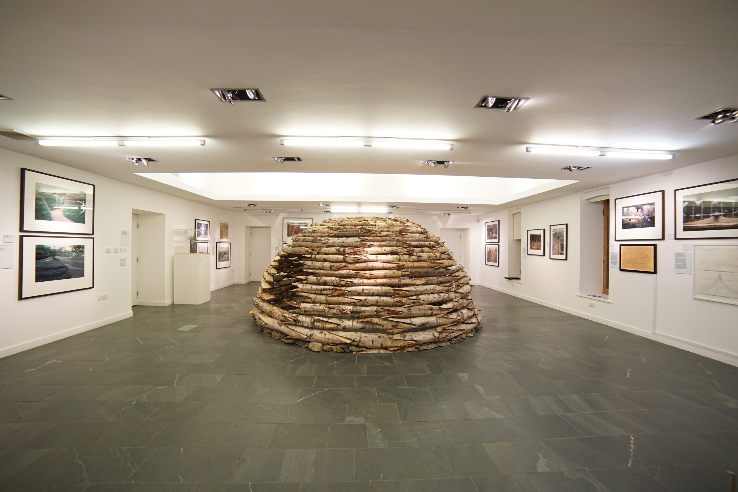 An igloo shaped hut made of wooden logs in the middle of a white walled gallery space
