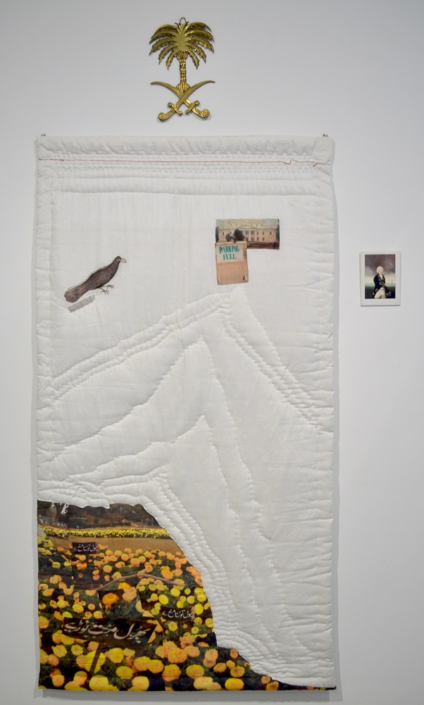 An embroidered white textile hangs on a white wall with fragments of blackbirds and farmers fields stitched on.