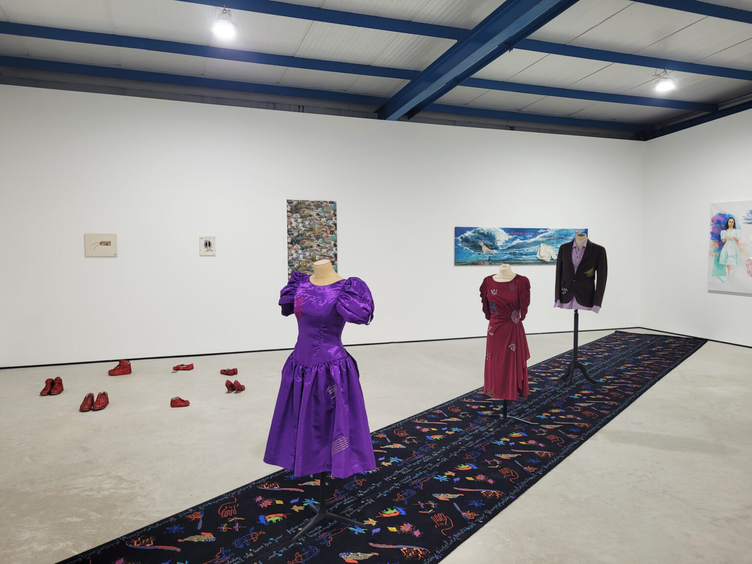 In the centre of the space is a long black carpet with multicoloured patterns, and three clothed dressmaker's mannequins.
