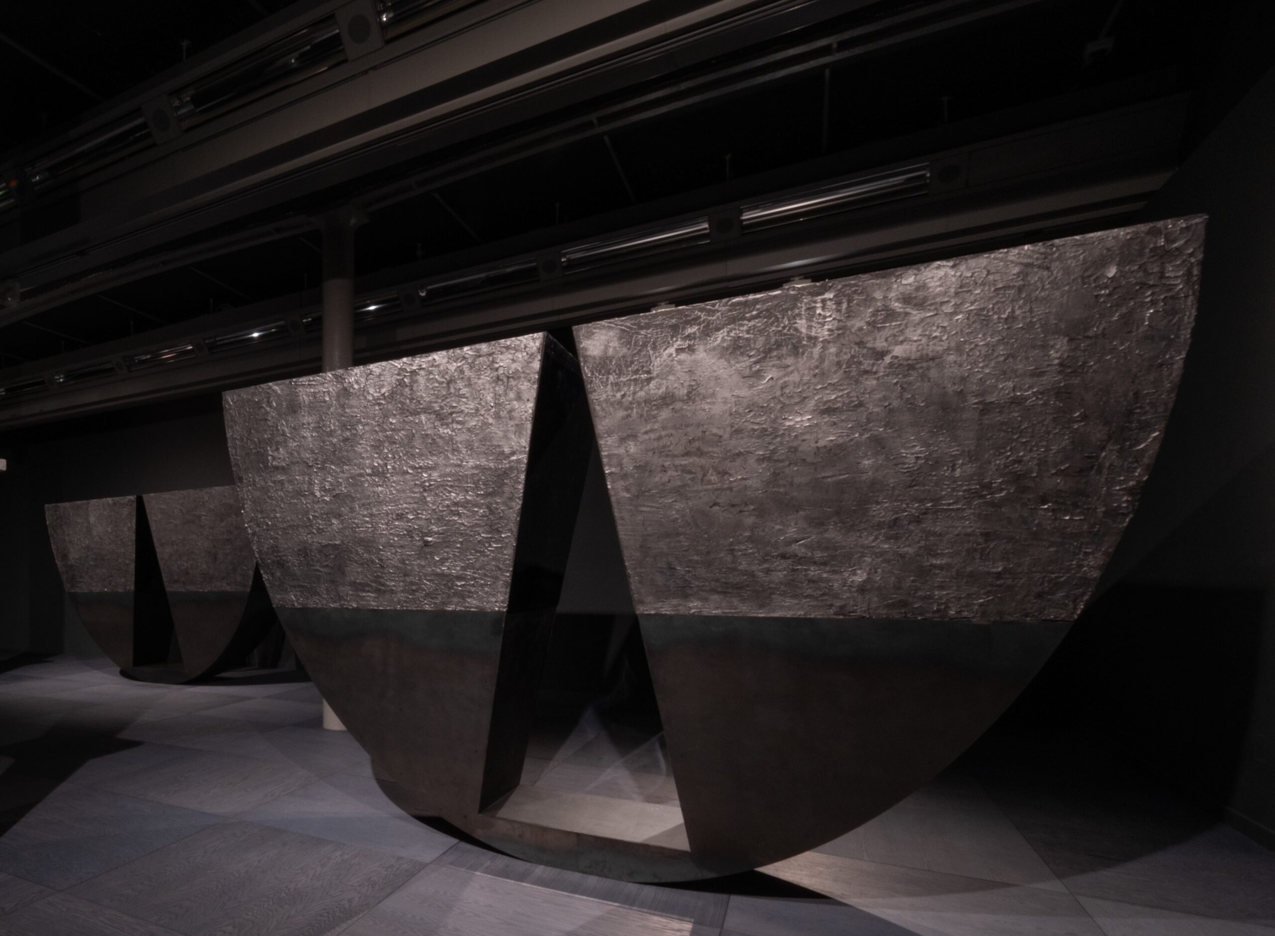 In a dark room two huge black sculptures of a semicircular shape with a triangular gap at the bottom.