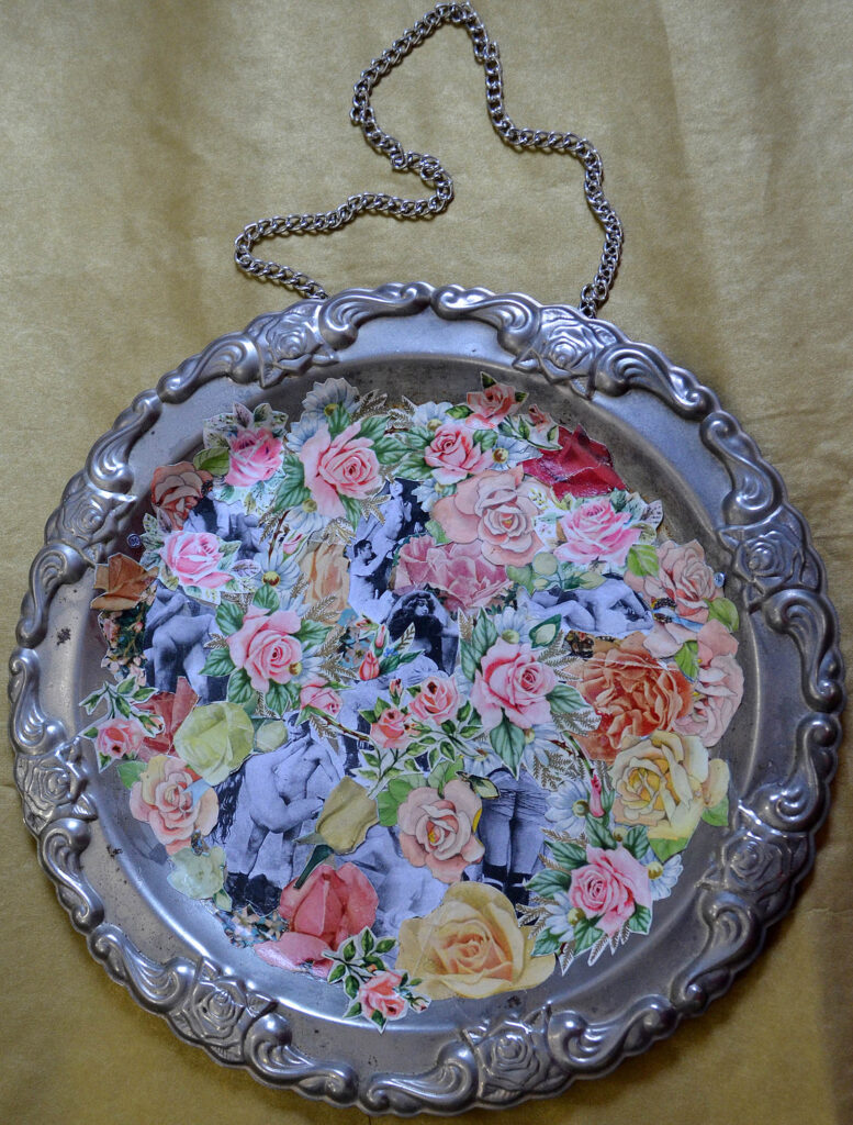 An ornament with a silver frame and a chain to hang from which is collaged with images of flowers and bodies.