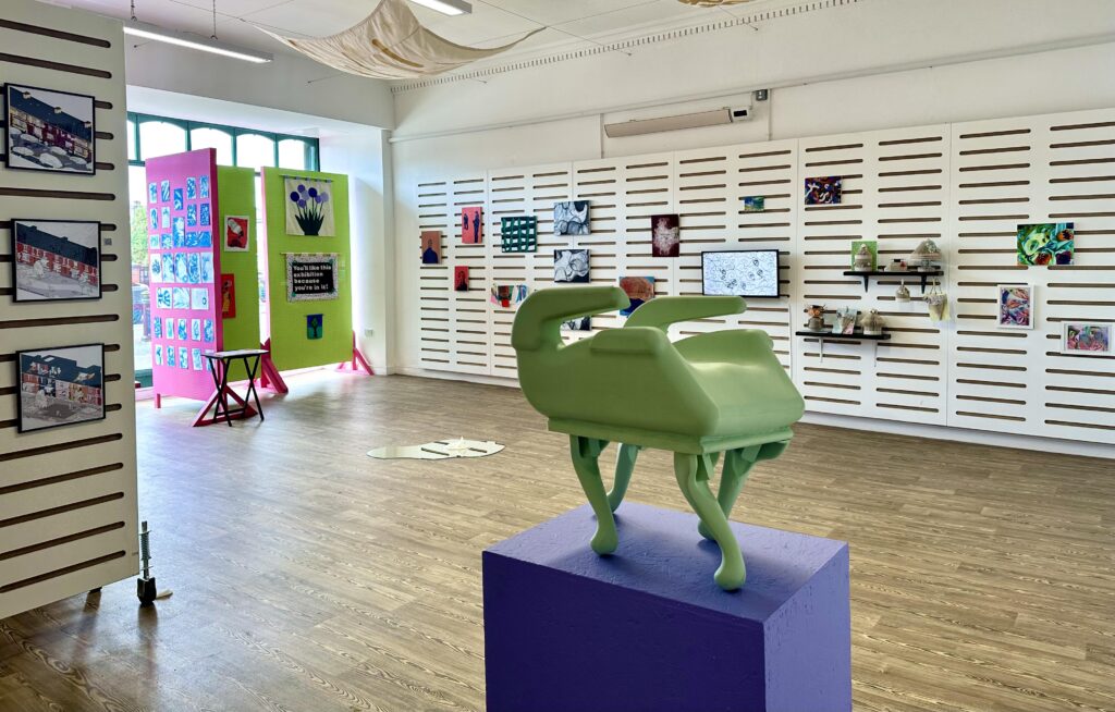 A shot of the gallery with a small green sculpture on four legs on a blue plinth in the foreground.