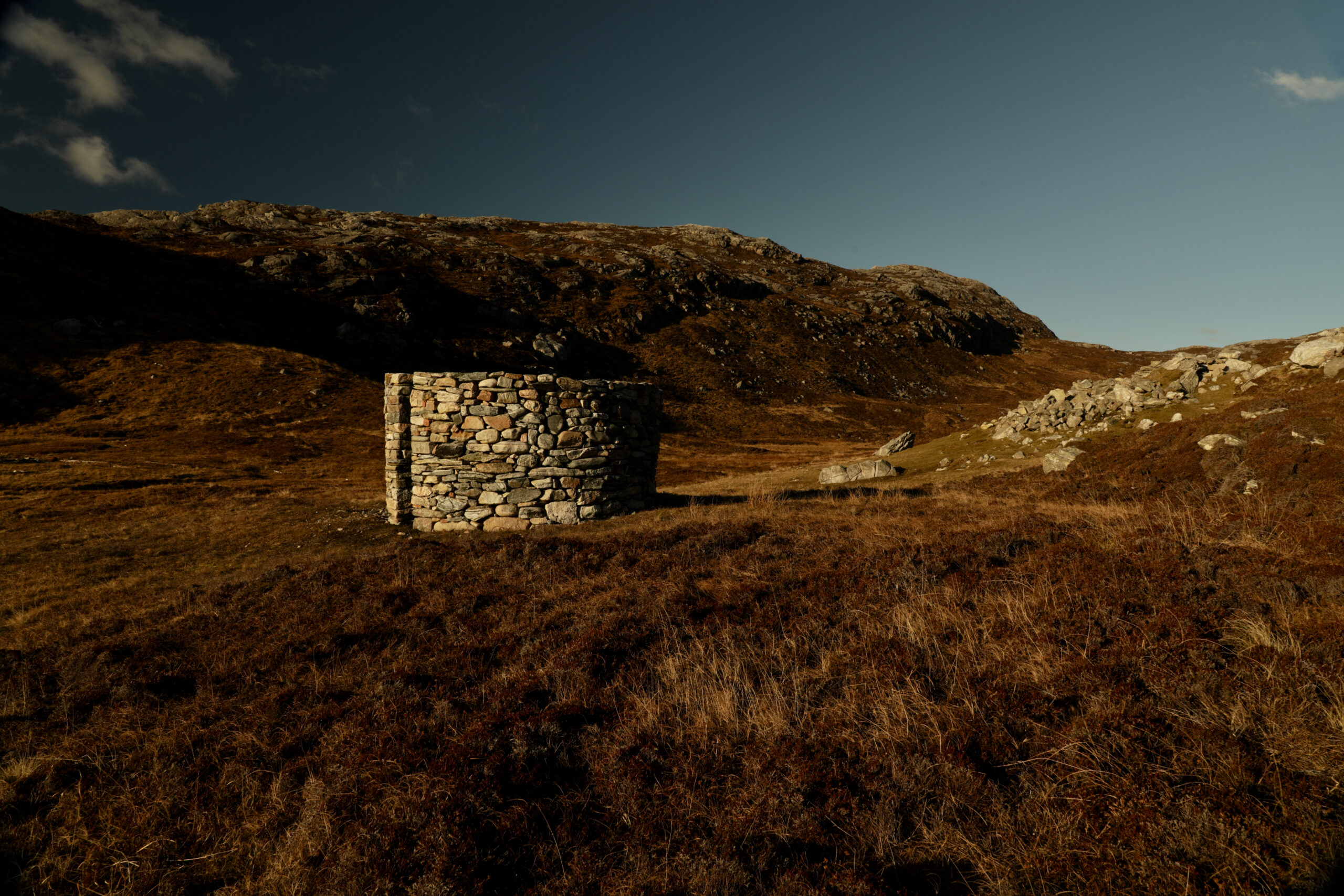 A short cylindrical tower built of fry stone wall in the outdoors under a blue sky