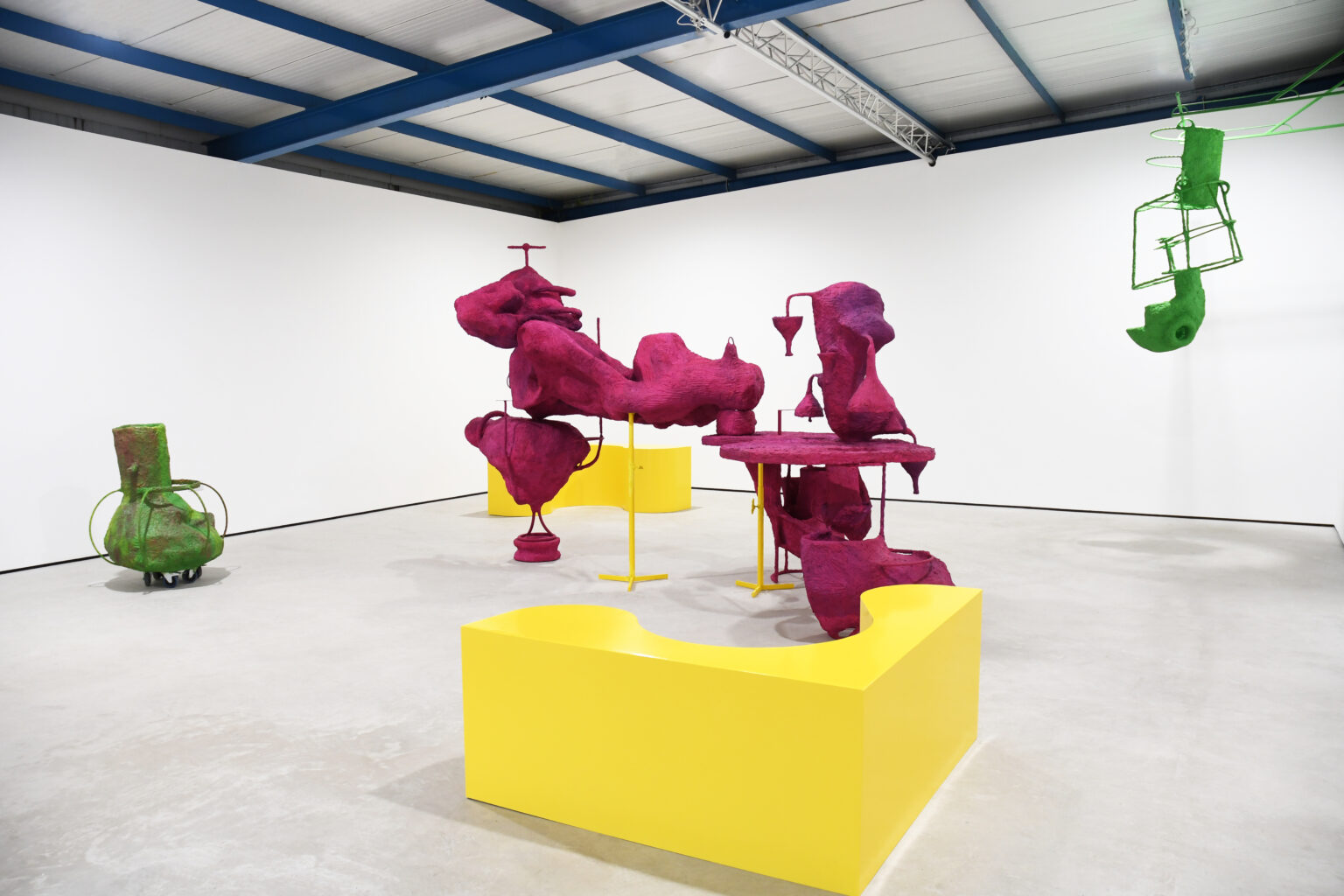 Sculptures that are bright yellow in the foreground and background, box shapes, and in the middle globular shapes on stands that are pinky-purple, kind of dada-ish, with two small green shapes to the left and right