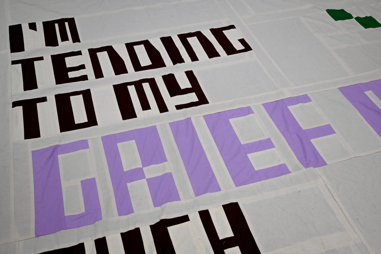 A textile work with text reading 'I'M TENDING TO MY GRIEF'