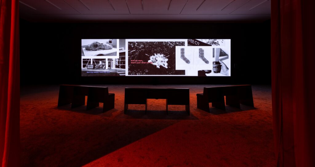 Three benches infront of a wide projection screen showing a collage of black and white images.