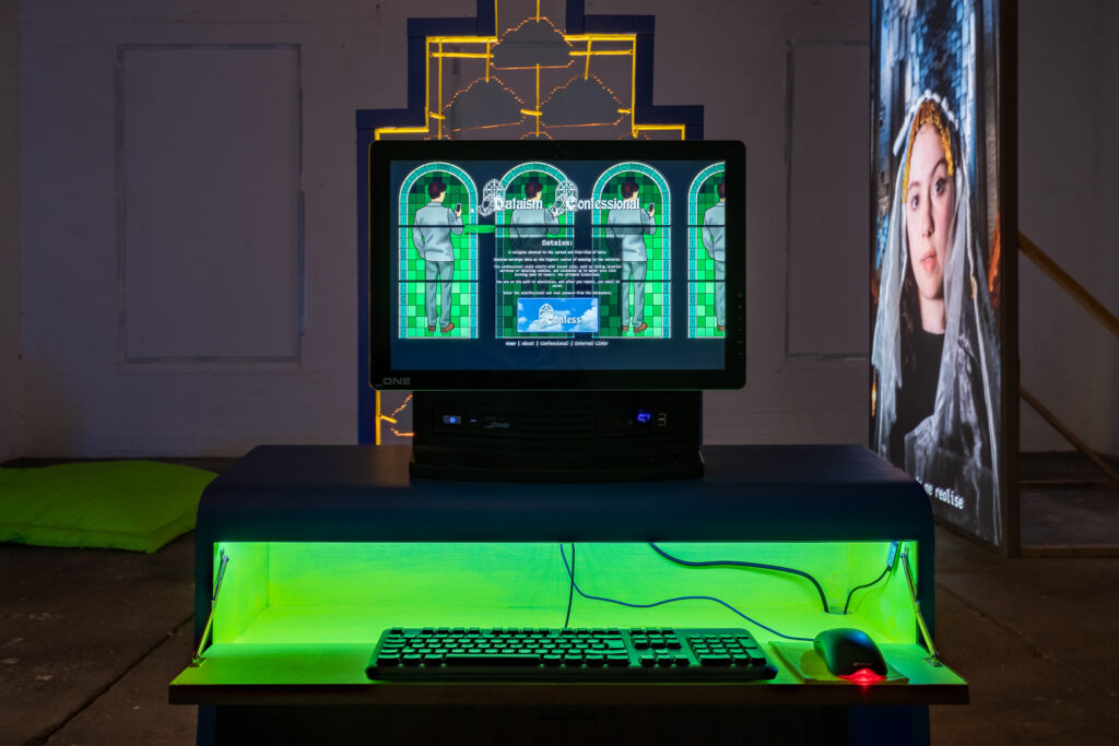 A computer terminal with green lighting, in a darkened room. The screen reads 'Dataism Confessional'.