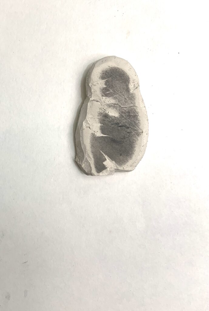 A white pencil eraser carved into the rough shape of a curled-up baby or foetus, its form further developed in graphite.