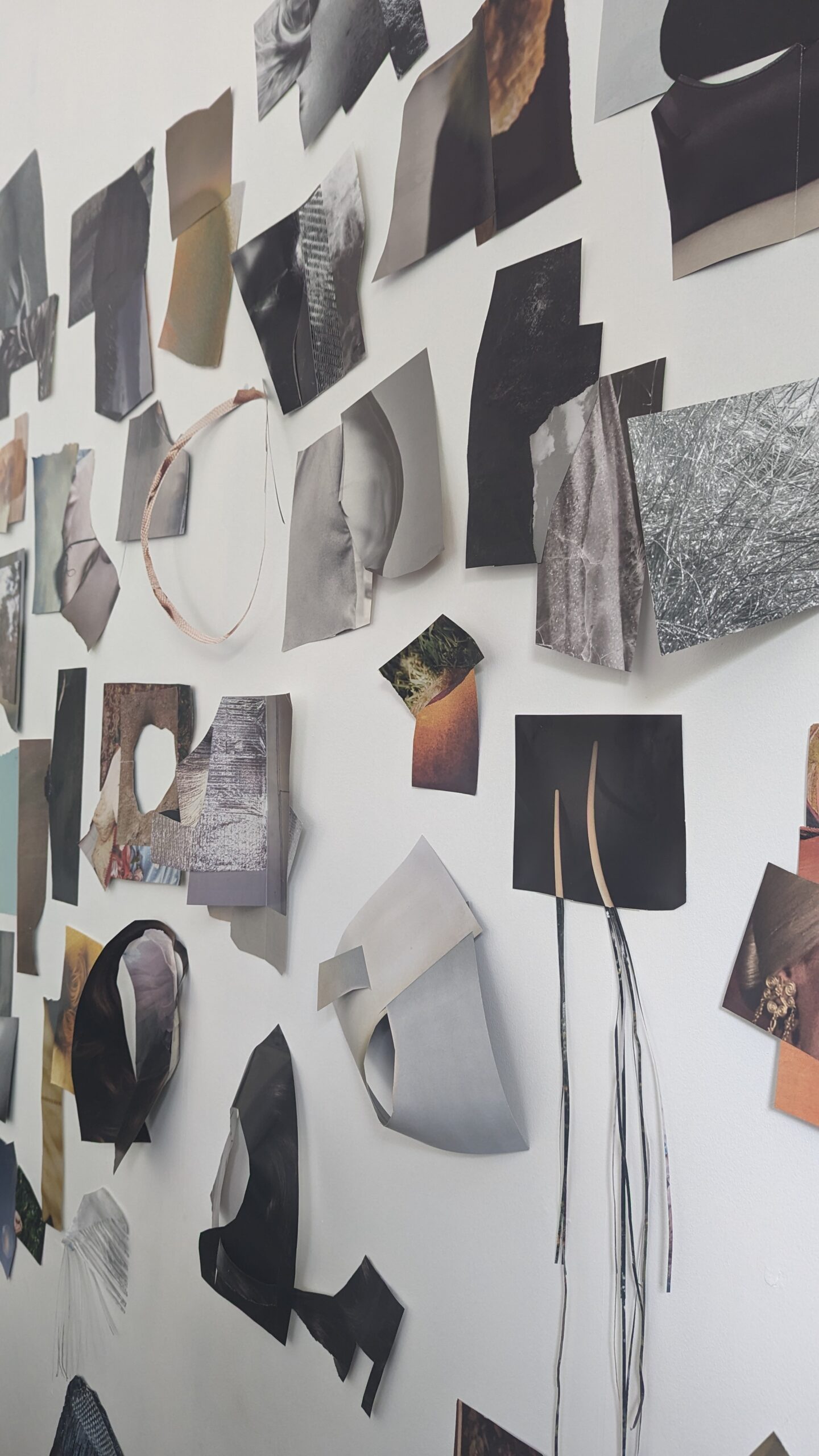 A white wall covered in little fragments of images on paper loosely attached in blacks, greys, whites and oranges