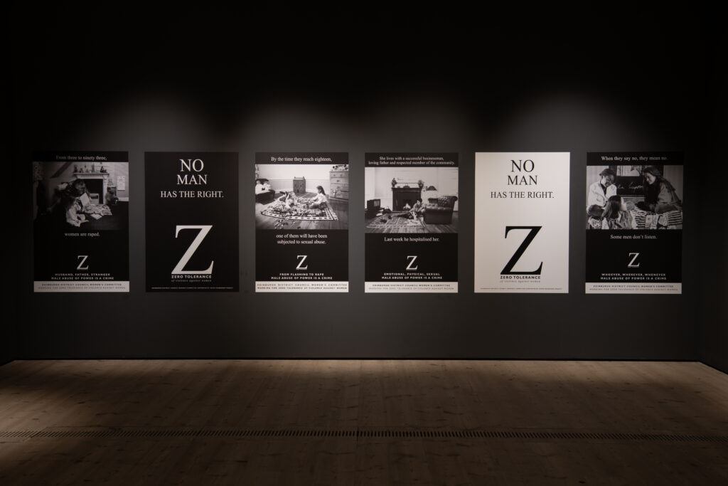 Six large black and white posters are displayed in a line on a black wall. They are all different versions of a Zero Tolerance campaign.