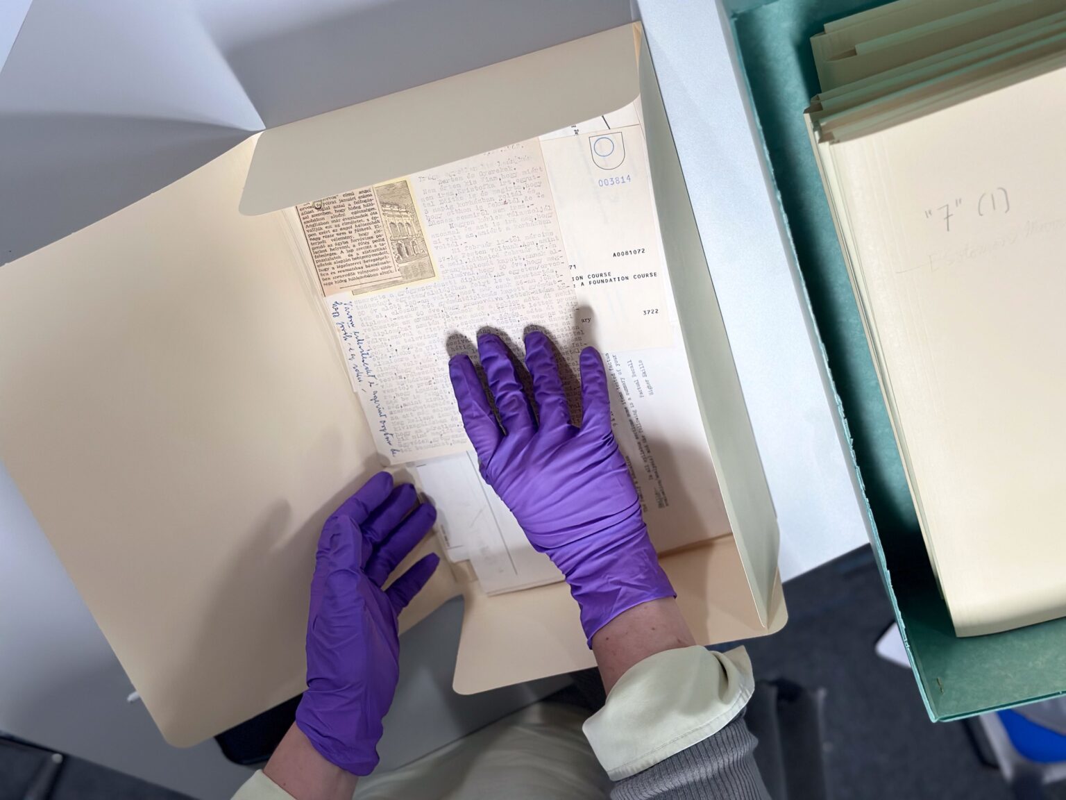 Hands in purple nitrile gloves handle delicate papers