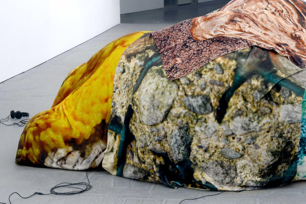 A close up on the corner of the mound with yellow, grey, mauve and peach fabrics, and the coiled headphones cables emerging from the bottom of the shape