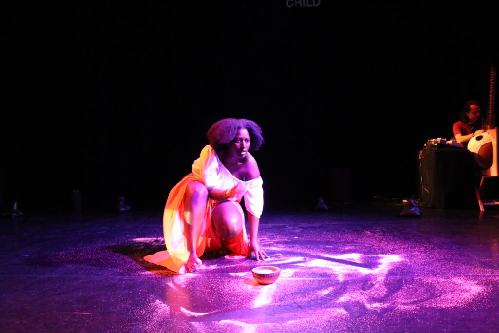 Camara crouched centre stage mid-speech, her right hand a blur of movement, left on the floor amid the white powder she's spread around