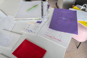 A table is spread with sheets of paper. The paper is marked with dots, lines and circles.