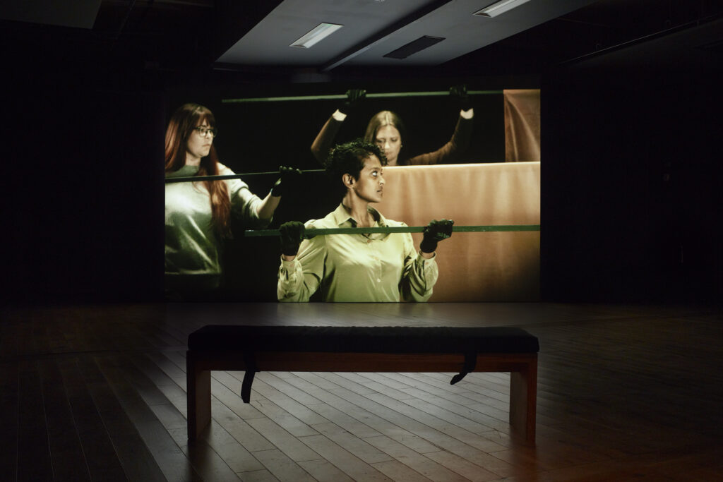 A dark room with huge screen where three gloved people hold long flagpoles across their bodies and face to the right