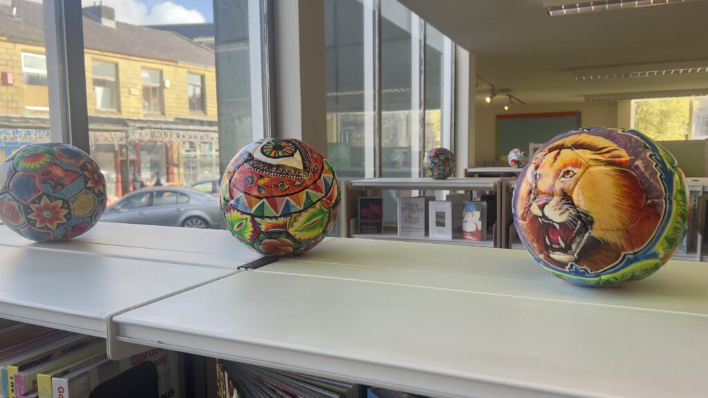 Three footballs on a shelf, brightly coloured with images of, left to right, flowers, an eye, a lion