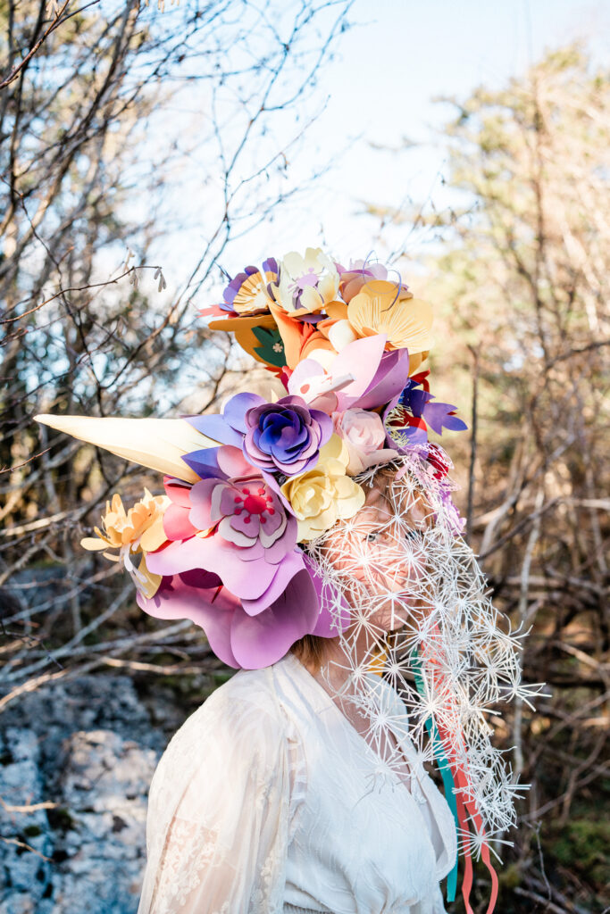 A crown and mask of brightly coloured paper flowers with a veil of wispy white petals