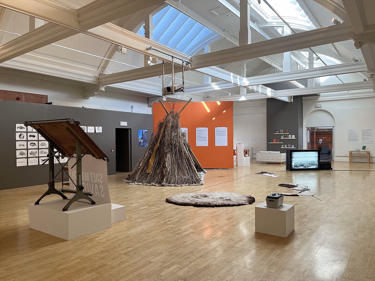 A big gallery space with a wigwam of sticks in the middle and various other works on plinths and the floor
