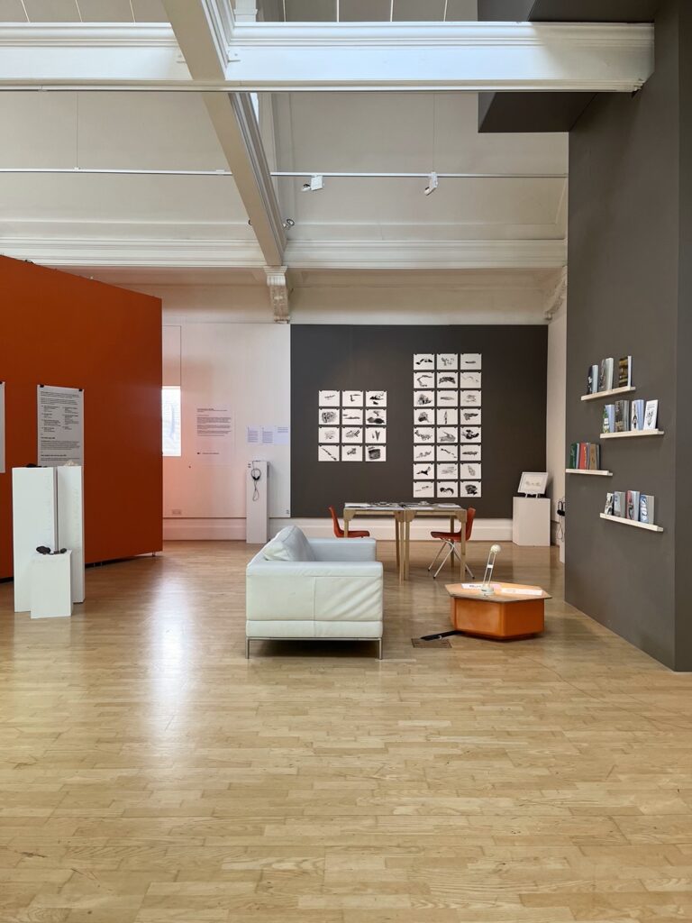 A long view of the gallery with a big sofa and on the back wall lots of square black and white images