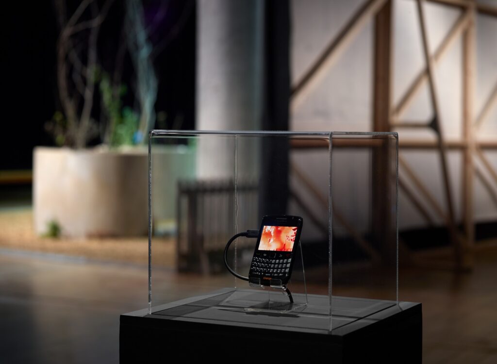 The blackberry handset in a vitrine with an image of orange flames on the screen