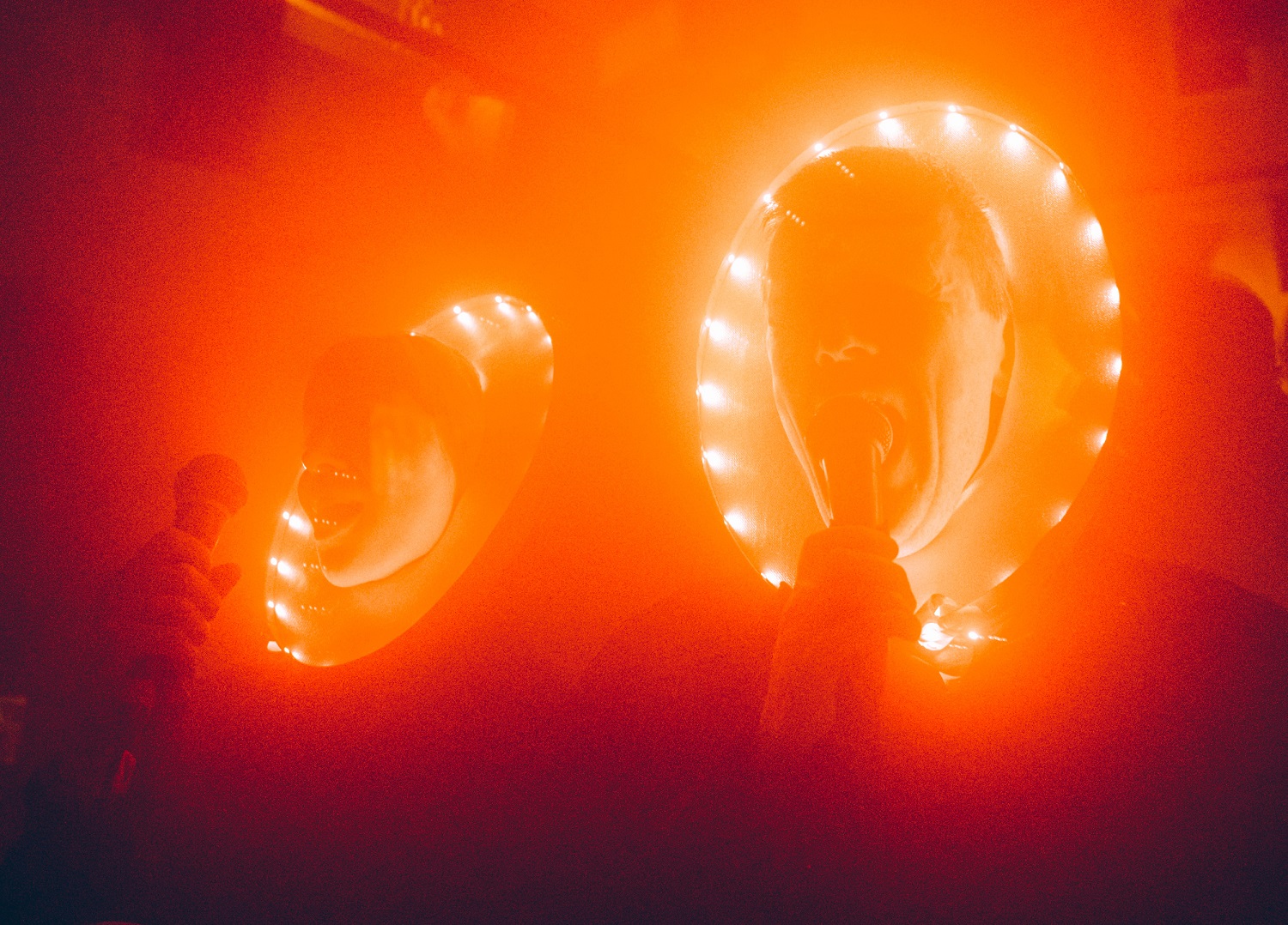 Two human faces lit with strings of fairy lights around them in a dark orange image