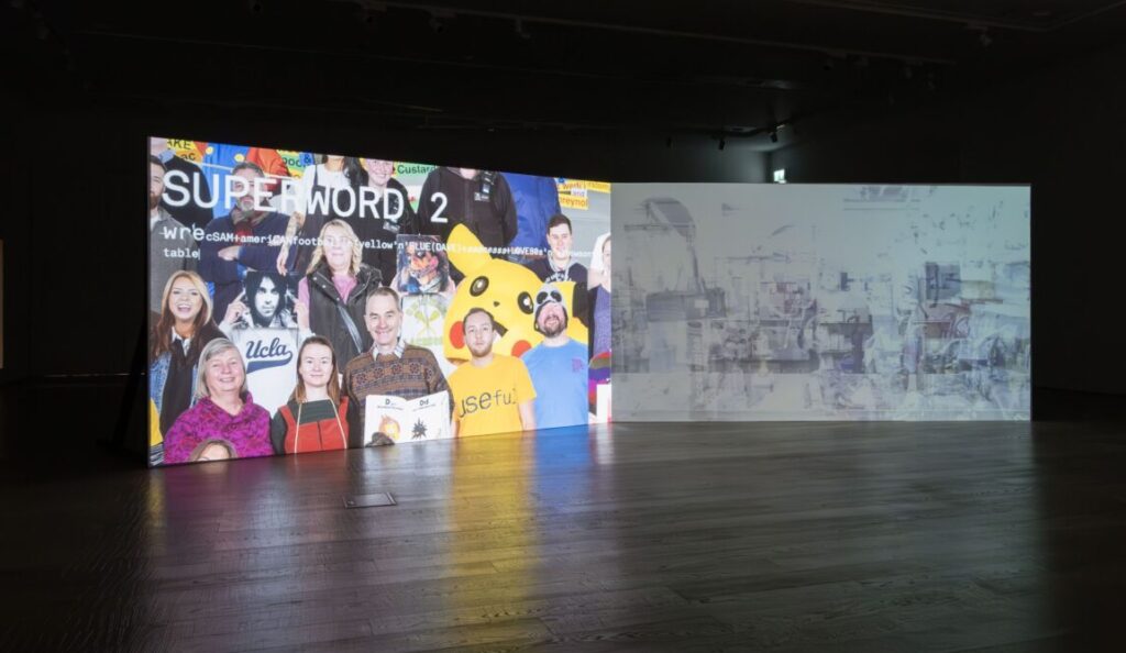 A dual channel film is projected onto a large screen in a gallery. The room is dark, lit only by the film.